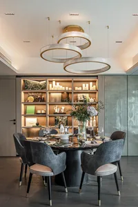 Modern dining room featuring a metal and carbon fiber table surrounded by upholstered chairs with gold accents, under a geome