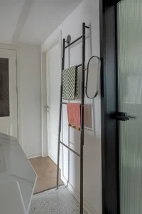 A minimalist bathroom with a modern metal towel rack holding checkered and pink towels.