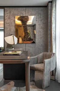 A minimalist office featuring a wooden desk, a leather-covered armchair, and a fabric-covered curtain, with a lamp and a book