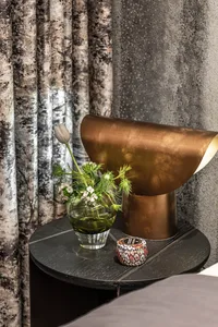 A stylish metallic bedside table with a vase of flowers and a small ornamental object in a bedroom setting.