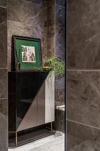 Modern bathroom interior with marble walls and floor, featuring a black and white geometric cabinet with a plant and framed a