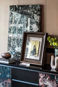 A framed antique resting on a black cabinet with decorative patterns.