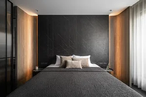 Modern minimalist bedroom with black marble walls and a neatly made bed with multiple pillows.