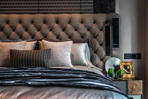 Modern bedroom with a leather headboard, decorative pillows, and green vases on the nightstand.