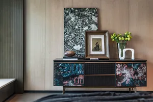 A modern living room featuring a black storage unit with colorful designs, positioned against a wooden wall with framed art.