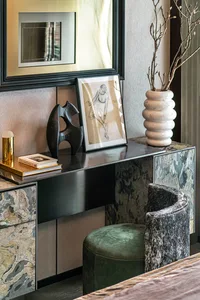 A modern bedroom featuring a marble dresser with a velvet upholstered stool and a framed drawing on the wall.