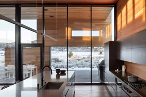 A modern residential kitchen featuring pine wood and large glass windows.
