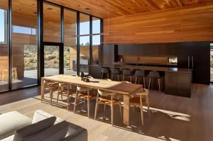 A modern residential kitchen with wooden flooring, cabinetry, and a large dining table.