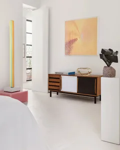 A modern bedroom featuring a bed, side cabinet, and abstract art, with a door leading outside.