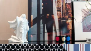 A white ceramic statue with flowing fabric on a multicolored checkered and striped surface.