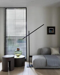 A minimalist living room featuring concrete and metal materials, with a grey couch, a black floor lamp, and a modern side tab