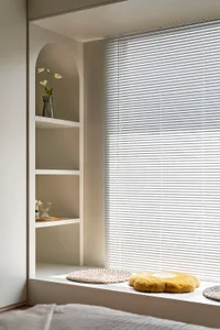 Window sill with minimalist setup including aluminum blinds, cushions, and woven mats.