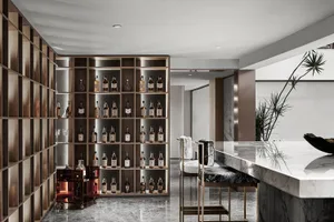 A modern bar with wooden shelves filled with bottles, a marble countertop, and concrete accents.