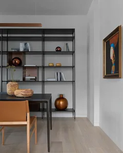 A modern dining room featuring a black shelf unit with metal frames, wood flooring, and ceramic vases.