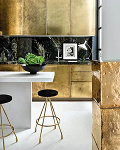 A modern kitchen interior with metallic gold cabinets, dark marble countertops, and a white island.