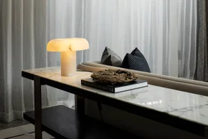 A modern living room with a marble coffee table, a mushroom-shaped table lamp, and a book with a sculpture on top.