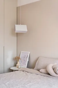 Bedroom with a minimalist design featuring a bed, pillows, a bedside lamp, and a vase with dried flowers on a small table.