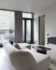 A modern living room with neutral-toned decor, minimalist design, and large windows with blinds.