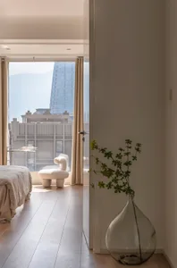 A modern residential interior with a white floor, beige curtains, and a glass vase with green plants.
