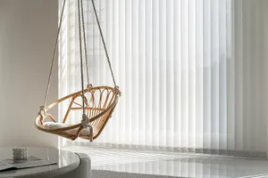 A modern, textured canvas chair hanging in a contemporary living room with vertical blinds allowing natural light to filter i