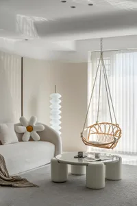 A minimalist interior design featuring a white concrete floor, wool sofa, glass lamp, and rattan hanging chair.