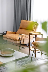 A minimalist living room featuring a leather armchair and sofa, with a glass coffee table and a green plant in the foreground