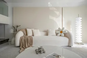 A minimalist living room with a white fabric sofa, cushions, and a round table.