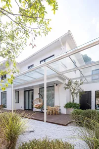 Modern patio with a glass roof and wooden deck, featuring minimalist design elements.