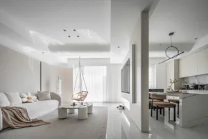 A minimalist white marble living room with a sofa, hanging chair, and kitchen area.