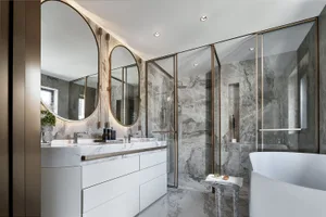 A modern bathroom featuring marble walls and flooring, a glass shower enclosure, and a white bathtub.