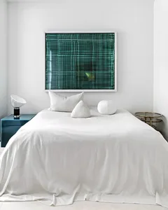 A modern bedroom with a green frame textile hanging above a neatly made bed.