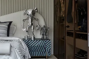 A modern monochrome bedroom featuring metallic sculptures on a patterned nightstand.