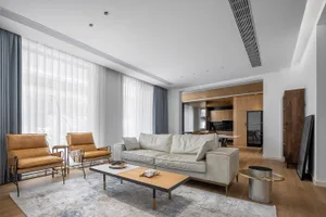 A modern living room with a neutral color palette featuring a white sofa, two brown armchairs, and a wooden coffee table.