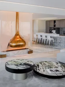 Modern lounge area with marble coffee tables, a glass pendant fireplace, and metal accents.
