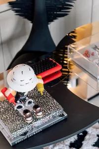 A modern interior design featuring a black round table with a patterned book, a toy figure holding ketchup bottle, and a clea
