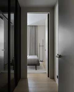 Minimalist bedroom with a grey upholstered bed, grey curtains, and wooden flooring.