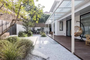 A modern residential exterior featuring a glass roof, white stone pavement, and wooden flooring.