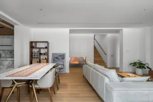 Modern dining room with white marble table and chairs, featuring a cozy fireplace and sleek white couch, surrounded by minima