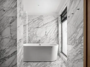 Modern bathroom with marble walls and floor, featuring a freestanding bathtub and a window.