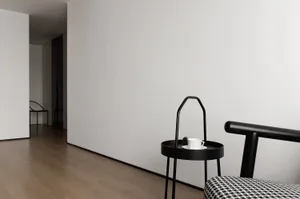 A minimalist white and black interior design with a steel side table and a patterned cushion.