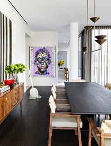 Modern dining room with a black wooden table, white cushioned chairs, and a colorful face painting.