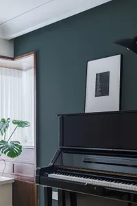 A modern interior design featuring a black piano in a well-lit room with green plant and framed artwork.
