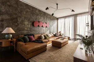 A modern living room featuring a leather sectional sofa and matching ottoman, with a textured wall, large windows, and a pott