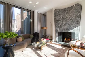A modern living room featuring a marble fireplace and a comfortable sofa with green pillows.