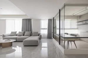 Modern living room featuring a grey sectional sofa, grey curtains, and a glass partition with a kitchenette.