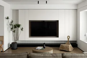Modern, minimalist living room with white walls, a black marble shelf, a round wooden coffee table, and a flat-screen TV embe