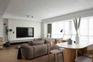 A modern living room featuring mixed materials with a focus on a large sectional sofa, white cabinets, and a white dining tab