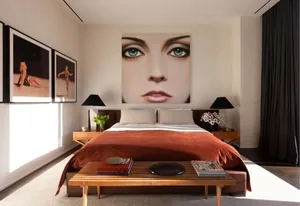 A minimalist bedroom with a large orange blanket, two black lamps, and a large portrait on the wall.