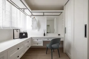 A minimalist white clothing closet with a hanging rod, drawers, and a desk area with a mirror and chair.