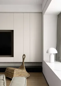 A modern minimalist living room with light-colored furniture, white cabinets, and a wicker bag on the floor.